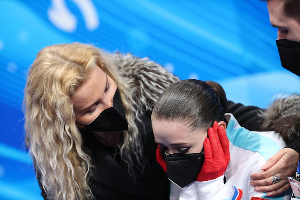 Kamila Valieva covers her ears as her coach speaks.