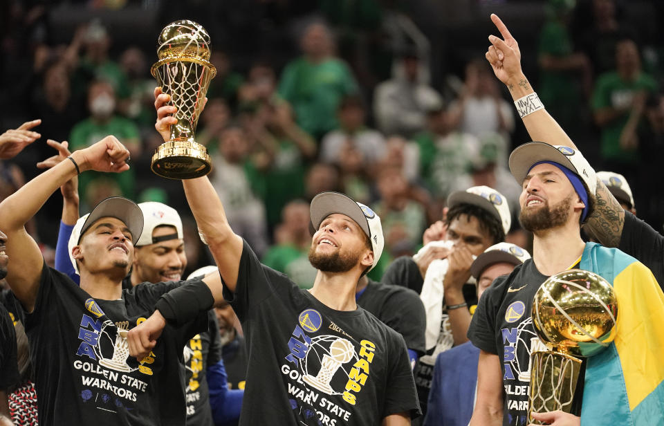 Golden State Warriors guard Stephen Curry, center, holds up the Bill Russell Trophy for NBA Finals Most Valuable Player after the Warriors defeated the Boston Celtics in Game 6 to the NBA championship on June 16, 2022, in Boston. (AP Photo/Steven Senne)