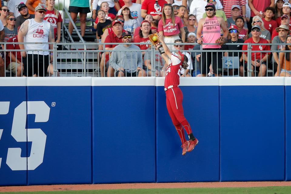 Oklahoma's Jayda Coleman (24) leaps over the wall to make a catch for an out in the first inning of the second game of the championship series in the Women's College World Series between the University of Oklahoma Sooners (OU) and the Texas Longhorns at USA Softball Hall of Fame Stadium in Oklahoma City, Thursday, June 9, 2022. 