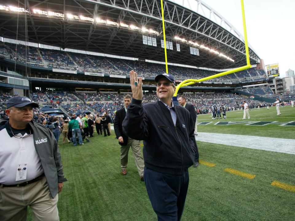 Paul Allen gestures to crowd while walking on field of Seattle Seahawks stadium