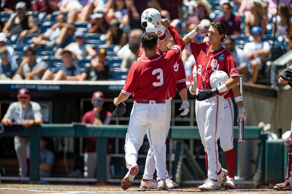 Oklahoma's Jimmy Crooks (3) bumps helmets with Peyton Graham (20) and Blake Robertson (26) celebrating his three run homer in the first inning against Texas A&amp;M during an NCAA College World Series baseball game Wednesday, June 22, 2022, in Omaha, Neb. (AP Photo/John Peterson)