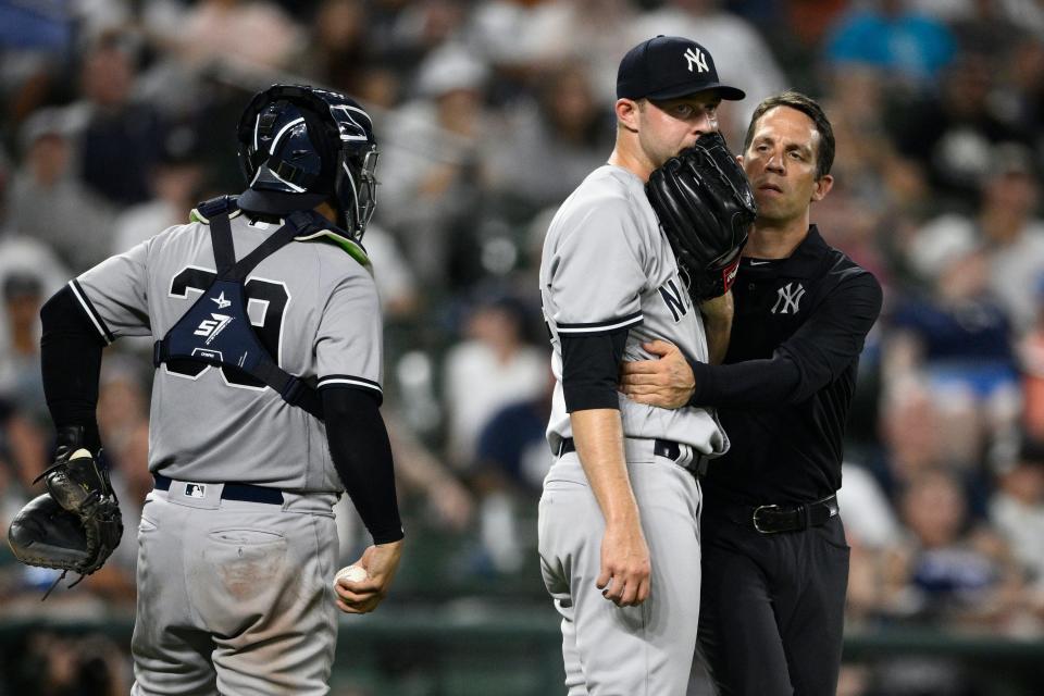 New York Yankees relief pitcher Michael King, center, is tended to by a trainer during the eighth inning of a baseball game against the Baltimore Orioles, Friday, July 22, 2022, in Baltimore. King left the game with an injury. New York Yankees catcher Jose Trevino is at left. The Yankees won 7-6.