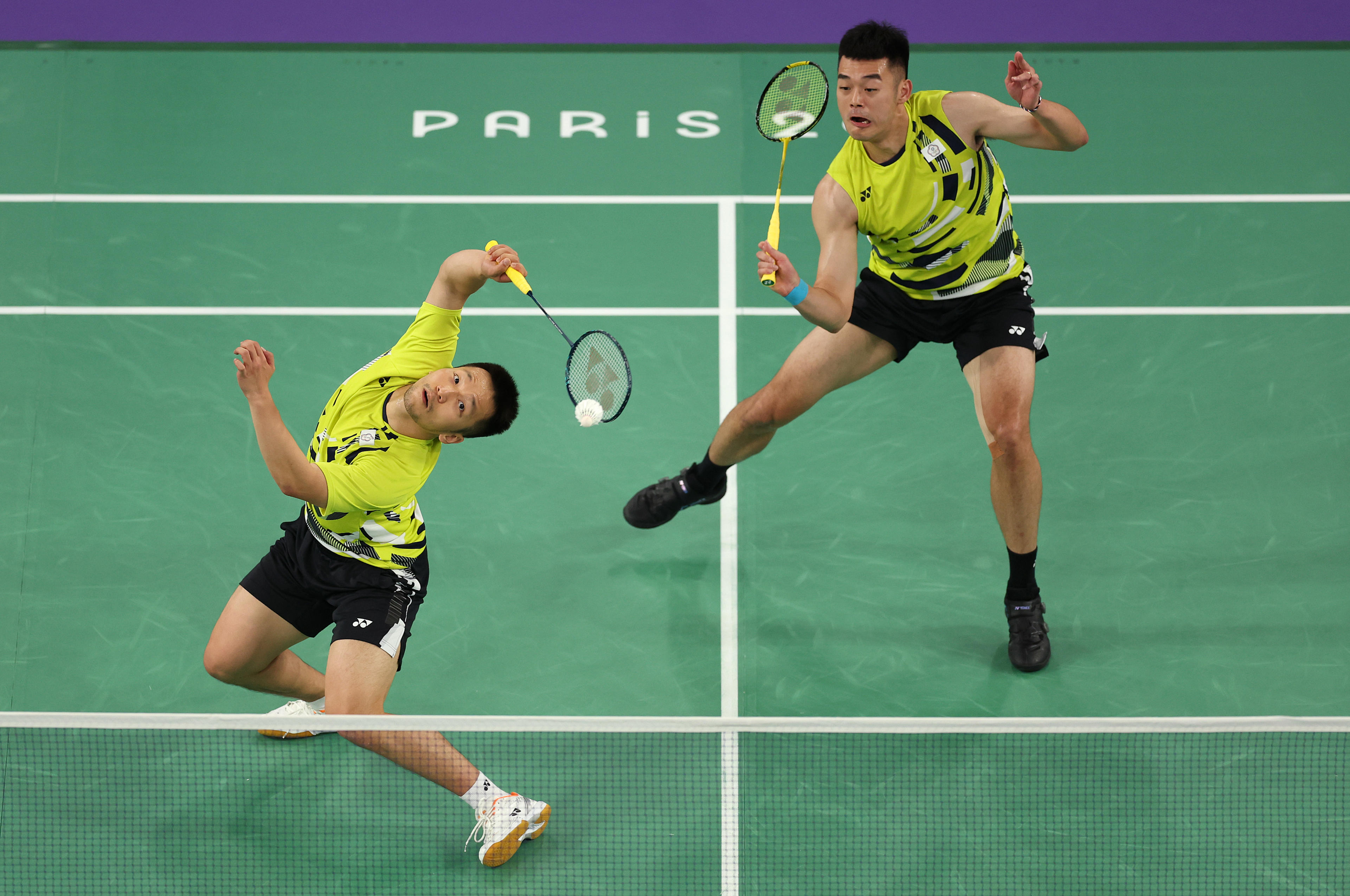 Yang Lee of Chinese Taipei plays a shot behind his head as Wang Chi-Lin watches during their semifinal match against Team Denmark on day seven of the Paris Olympics at Porte de La Chapelle Arena on August 02, 2024 in Paris, France. (Julian Finney/Getty Images)