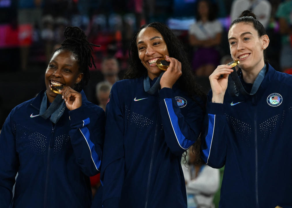 Gold medallists (From L) USA's #08 Chelsea Gray, USA's #09 A'ja Wilson and USA's #10 Breanna Stewart bite their medal as they celebrate on the podium after the women's Gold Medal basketball match between France and the USA during the Paris 2024 Olympic Games at the Bercy Arena in Paris on August 11, 2024. (Photo by Paul ELLIS / AFP) (Photo by PAUL ELLIS/AFP via Getty Images)