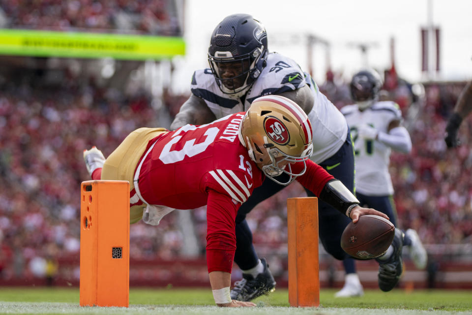 November 17, 2024; Santa Clara, California, USA; San Francisco 49ers quarterback Brock Purdy (13) scores a touchdown against Seattle Seahawks defensive tackle Jarran Reed (90) during the first quarter at Levi's Stadium. Mandatory Credit: Kyle Terada-Imagn Images