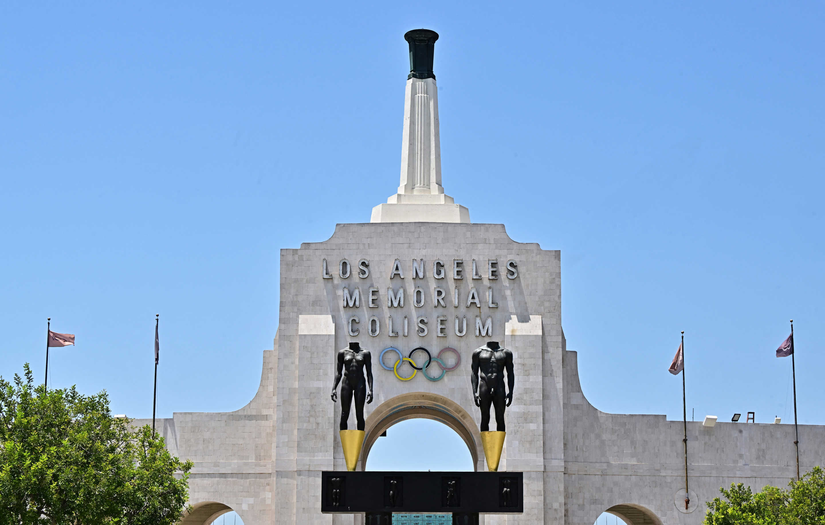 Flags fly in the wind at the Los Angeles Memorial Coliseum on July 18, 2024 in Los Angeles, California. Los Angeles will become a three-time Summer Olympic host city after hosting the 2028 Summer Olympics. (Photo by Frederic J. BROWN / AFP) (Photo by FREDERIC J. BROWN/AFP via Getty Images)