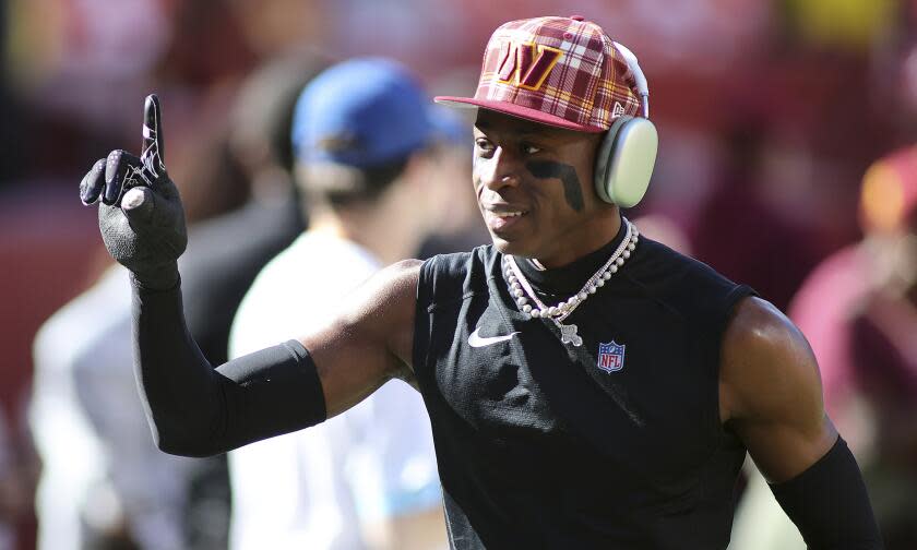 Washington cornerback Emmanuel Forbes Jr. (13) gives the No. 1 sign while wearing a Commanders cap.