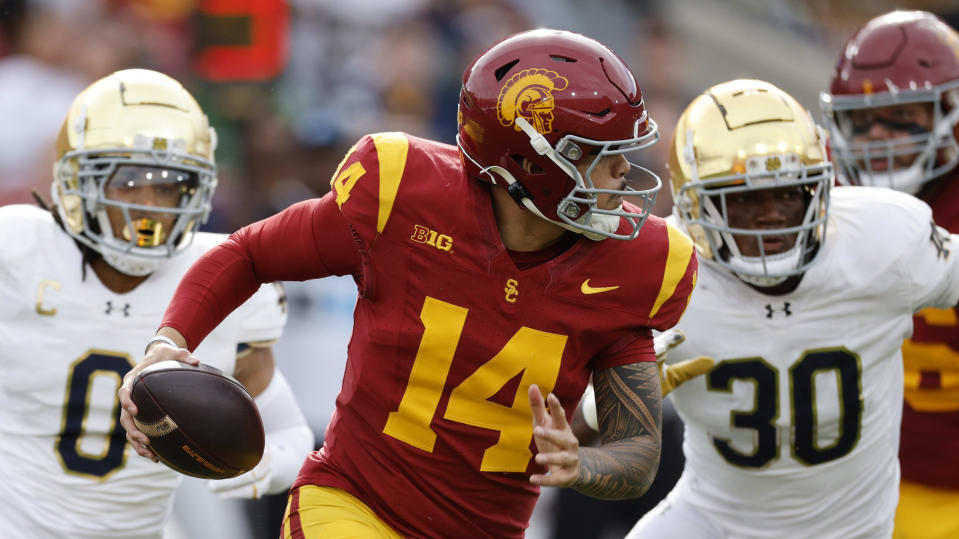 LOS ANGELES, CALIFORNIA - NOVEMBER 30: Quarterback Jayden Maiava #14 of the USC Trojans is chased out of the pocket by safety Xavier Watts #0 and defensive lineman Bryce Young #30 of the Notre Dame Fighting Irish during the first half at United Airlines Field at the Los Angeles Memorial Coliseum on November 30, 2024 in Los Angeles, California. (Photo by Kevork Djansezian/Getty Images)