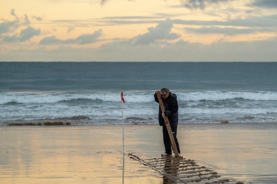 A delegate marks the lines of the field on the wet sand. (David Ramos/Getty Images)